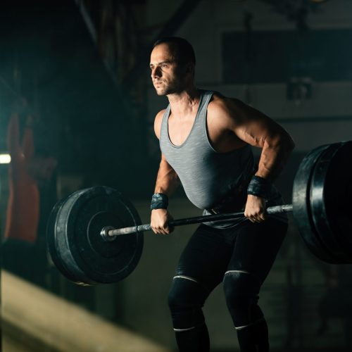 Athletic man exercising with barbell during cross training in health club.